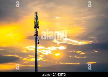 Un grand angle de visualisation d'un monopole de la tour site cellulaire au coucher du soleil. La silhouette en contre-jour d'or station de base de téléphonie cellulaire avec nuages épars et copy space Banque D'Images