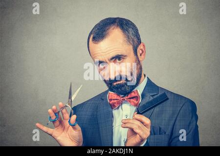 Coiffure barbu, portant veste élégante avec nœud Papillon rouge, qui posent avec ciseaux et peigne. Adultes élégant man studio portrait, isolée à gray backg Banque D'Images