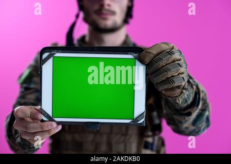 Soldat de l'armée montrant un ordinateur tablette avec un écran vert blanc isolé sur fond rose Banque D'Images