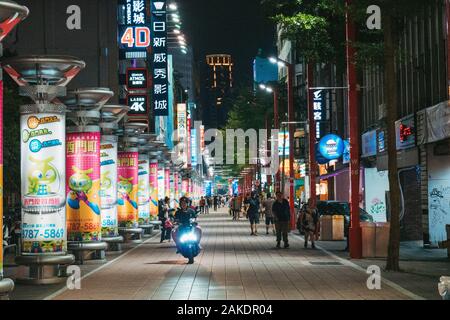 Un scooter descend dans un centre commercial piétonnier rempli de publicités illuminées la nuit, dans le centre de Taipei, à Taïwan Banque D'Images