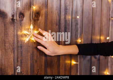 Woman's hand touching décoration de Noël étoile brillante sur le mur en bois. Concept de vacances de Noël Banque D'Images