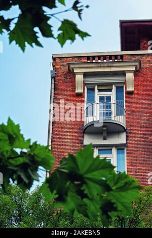Low angle view of un balcon sur un magnifique immeuble résidentiel avec brique rouge encadré par des branches d'arbre et de feuilles vertes.