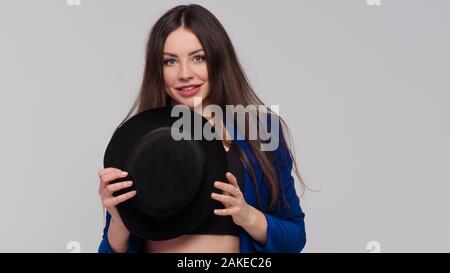 Brunette positive avec un chapeau, une fille moderne et branchée dans un costume bleu foncé. Portrait studio d'un arrière-plan gris clair. Banque D'Images