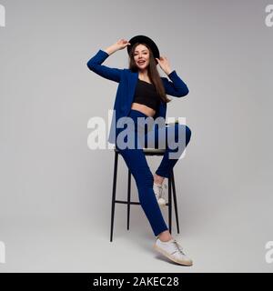 Femme d'affaires élégante dans un pantsuit bleu foncé. Brunette positive avec un chapeau, une fille branchée et moderne. Banque D'Images