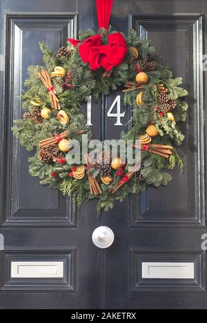 Les bâtons de cannelle et pomme de pin couronne de Noël accroché sur une porte en bois Banque D'Images