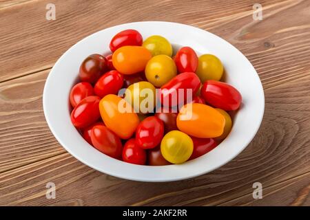 Savoureux mélange de tomates cerises multicolores dans un bol en porcelaine blanche sur une table en bois brun. Des légumes, des plats végétariens et une saine alimentation. Régime cru de nourriture. Banque D'Images
