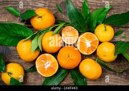 La mandarine, des mandarines, clémentines fruits orange avec des feuilles sur fond de bois. Mandarines fraîches, feuilles vertes avec des gouttes d'eau. Vue d'en haut Banque D'Images