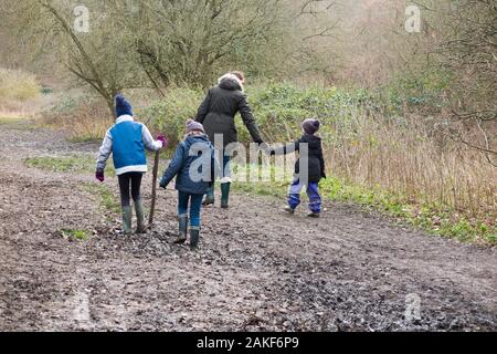 Mère / maman / maman marchant dans la boue avec ses trois enfants un jour d'hiver sur un chemin boueux à travers les bois de bois sur West End Common, Esher, Surrey. ROYAUME-UNI. (115) Banque D'Images