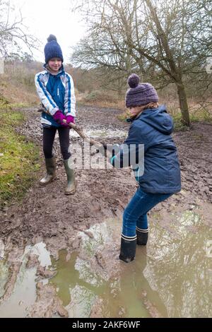 Deux jeunes filles / filles / sœurs de neuf ans et de 7 ans, portant des bottes Wellington, aime aider, sauver et jouer dans une grande flaque mouillée pendant une promenade en famille au-dessus de West End Common, Esher, Surrey. ROYAUME-UNI (115) Banque D'Images