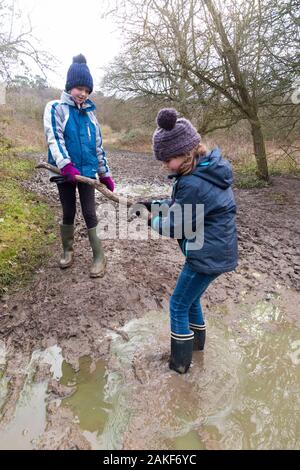 Deux jeunes filles / filles / sœurs de neuf ans et de 7 ans, portant des bottes Wellington, aime aider, sauver et jouer dans une grande flaque mouillée pendant une promenade en famille au-dessus de West End Common, Esher, Surrey. ROYAUME-UNI (115) Banque D'Images