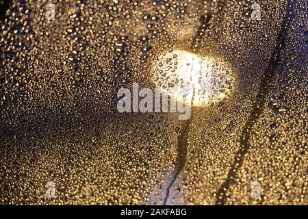 Moody photo de gouttes lumineuses scintillantes sur le verre en face d'une lampe de rue dans la nuit. Vu sur un jour de pluie en Allemagne en janvier, d'une fenêtre de toit Banque D'Images