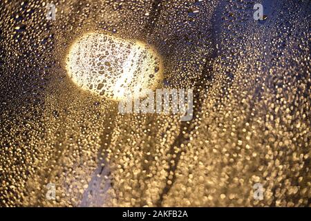 Moody photo de gouttes lumineuses scintillantes sur le verre en face d'une lampe de rue dans la nuit. Vu sur un jour de pluie en Allemagne en janvier, d'une fenêtre de toit Banque D'Images