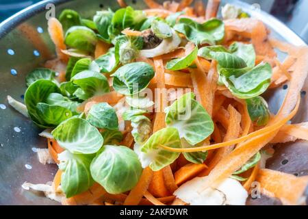 Graines et de pelures de légumes carotte dans une passoire métallique dans une cuisine dans le cadre de la préparation d'un repas. Banque D'Images