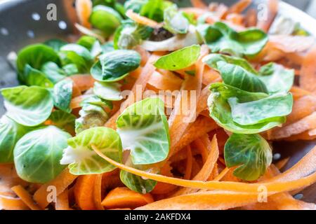 Graines et de pelures de légumes carotte dans une passoire métallique dans une cuisine dans le cadre de la préparation d'un repas. Banque D'Images