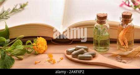 La médecine traditionnelle pour la préparation de médicaments avec capsules et de guérison des essences et des livre sur table en bois. Vue de face. Vue panoramique compos Banque D'Images