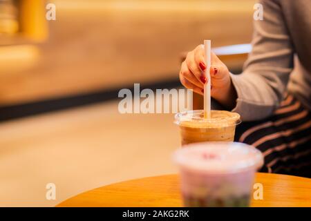 La femme avec le papier de la paille dans le verre en plastique de café froid. Banque D'Images