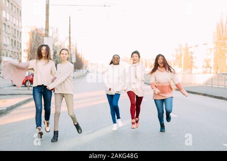 Groupe multiracial d'amis de cinq jeunes femmes s'exécute et a un amusement on city street. Le concept de l'amitié et l'unité entre les différentes race humaine Banque D'Images