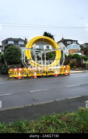 Une grande bobine de tuyau jaune garé au bord de la route entourée de barrières de sécurité à Newquay en Cornouailles. Banque D'Images