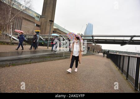 Londres, Royaume-Uni, 9 janvier 2020, Météo. Après-midi sombre dans la ville, avec de fortes pluies qui s'y déménage. Une femme avec un parapluie coloré passant devant le pont du Millénaire et le Tate Modern Banque D'Images