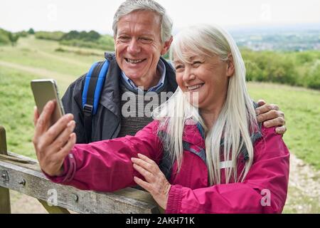 Happy Senior Couple Hiking in Countryside debout près de la porte et en tenant le téléphone mobile Selfies Banque D'Images