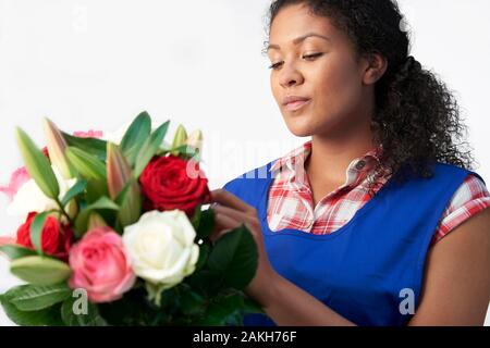 Femme Floriste Organisant Bouquet De Lillies Et De Roses Contre Fond Blanc Banque D'Images