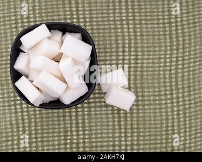 Morceaux de sucre raffiné blanc, cubes, dans un bol sur le tissu de fond avec copyspace. Banque D'Images