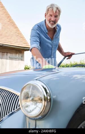 Portrait d'homme mûr restauré Polissage Voiture de sport classique dehors à la maison Banque D'Images