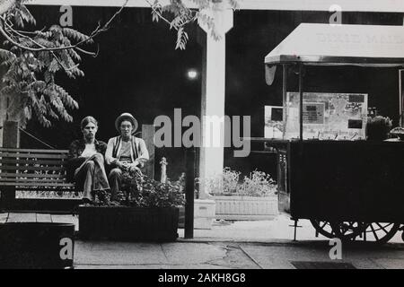 Belle photographie noir et blanc des années 1970 de deux hommes assis sur un banc de parc Banque D'Images