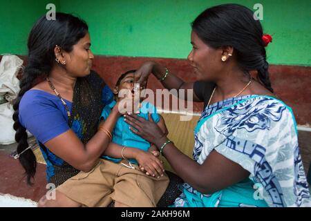 Légende : la santé sociale accrédités (ASHA) Gurushanthi administre le vaccin contre la poliomyélite à Mahendra tandis que sa mère le tient. Grâce à l'Chamko Banque D'Images