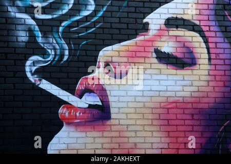 Femme fumant de l'art de la rue de cigarette dans la région de Digbeth à Birmingham, Angleterre, Royaume-Uni. Banque D'Images