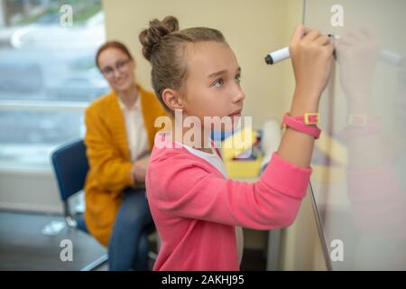 Fille concentré écrit sur le tableau blanc à l'école Banque D'Images