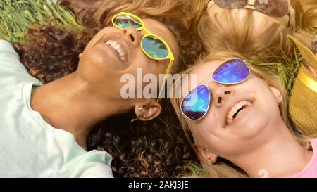 Close-up de visages amis, happy girls lying on grass, amitié multiraciale Banque D'Images