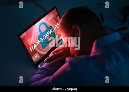 Inquiets Businessman Looking At Laptop avec Ransomware mots à l'écran sur le lieu de travail Banque D'Images