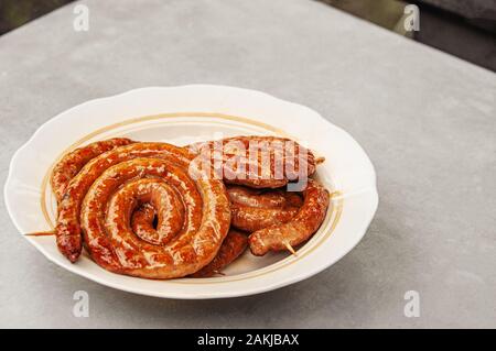 Saucisse faite maison, cuits sur le grill. Saucisses fines enroulé se trouvent sur une plaque sur la surface de la table. Copier l'espace. Focus sélectif. Banque D'Images