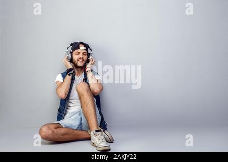 Dans le rythme de ma musique. Ambiance jeune homme barbu dans les écouteurs assis près de mur gris et l'écoute de la musique. Banque D'Images