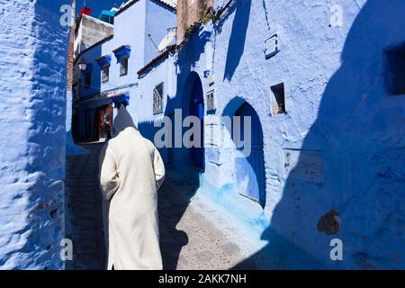 Un homme seul portant djellaba lumineux avec un capuchon qui couvre la tête de marcher dans la rue de la médina de Chefchaouen (également connu sous le nom de Chaouen), Maroc Banque D'Images