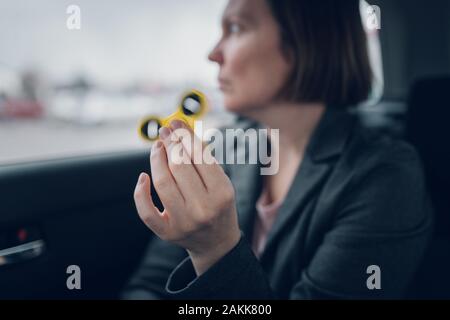 Businesswoman jouant avec fidget spinner dans la voiture pendant qu'assis à l'arrière du véhicule et se rendre à son travail, selective focus Banque D'Images