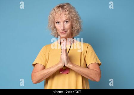 Namaste, que la paix soit avec vous. Portrait of happy young woman avec des cheveux blonds en t-shirt jaune, tenant les mains de prier sur la poitrine et tout en souriant Banque D'Images