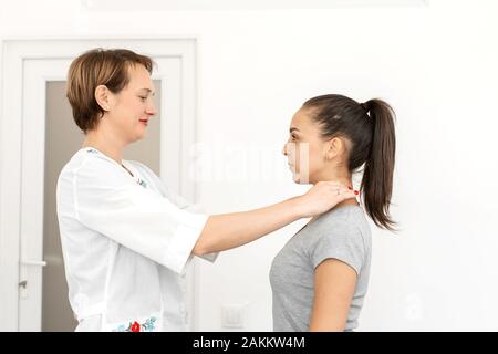 Jeune femme aux cheveux courts professionnels thérapeute dans un cabinet médical, examine un patient, sent la glande thyroïde. Banque D'Images