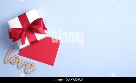 Happy Valentines Day concept. Boîte cadeau blanche avec Red Ribbon bow, enveloppe rouge, signe de l'amour sur fond bleu pastel. Mise à plat, vue du dessus, copiez l'espace. B Banque D'Images