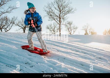 Photo d'action d'une fille debout sur un traîneau descendant une colline en hiver. Banque D'Images