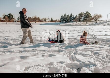 Vue latérale de l'homme tirant deux filles sur un traîneau à travers le champ en hiver Banque D'Images