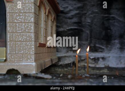 Deux bougies fines illuminées dans une cheminée spéciale à côté du petit modèle de l'église orthodoxe, la tradition dans le christianisme oriental. Banque D'Images