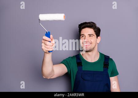 Portrait de la maison de l'homme de travail confiant positive peinture salle avec rouleau blanc rénovation appartement porter vert t-shirt bleu uniforme combinaisons isolées Banque D'Images