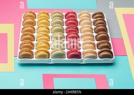 Un dessert classique français. Macarons colorés bleu jaune rose créatif sur fond gris empilés dans une boîte, selective focus Banque D'Images