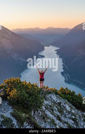 Le coucher du soleil, jeune femme à la recherche de paysage de montagnes s'étend les bras en l'air, vue de la montagne à Baerenkopf Lac Achensee, Tyrol, Autriche Banque D'Images