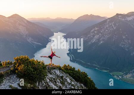 Le coucher du soleil, jeune femme étend les bras en l'air, vue de la montagne Baerenkopf à gauche, le lac Achensee et Seebergspitze Seekarspitze Rofan, droite Banque D'Images