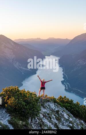 Le coucher du soleil, jeune femme étend les bras en l'air, vue de la montagne Baerenkopf à gauche, le lac Achensee et Seebergspitze Seekarspitze Rofan, droite Banque D'Images