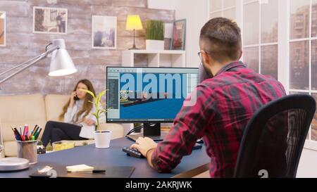 Au-dessus de l'épaule de jeune développeur de jeu travaillant à la maison tandis que sa petite amie marche dans le backgorund Banque D'Images