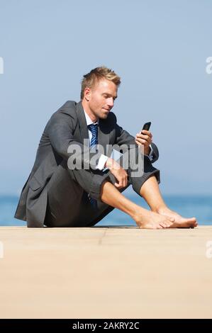 Barefoot détendue businessman sitting on a sunny dock en utilisant son smartphone Banque D'Images